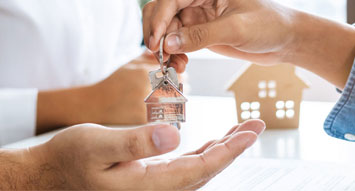 A photo three hands depicting landlords insurance, one is turning over a key to another hand and the other one is laying on the top of a table with a house miniature.